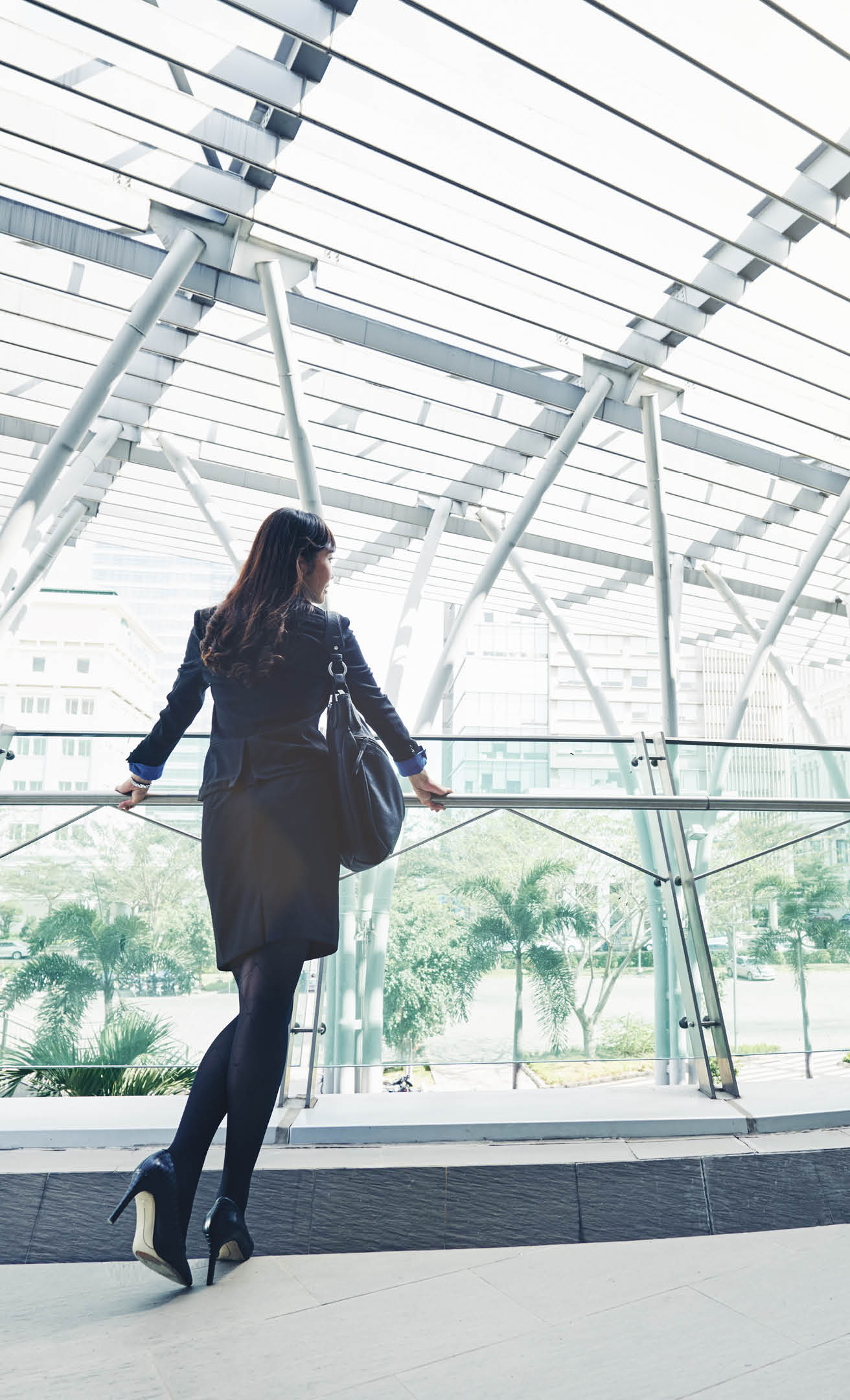 Rear view of young business woman standing on indoor balcony in the office building
