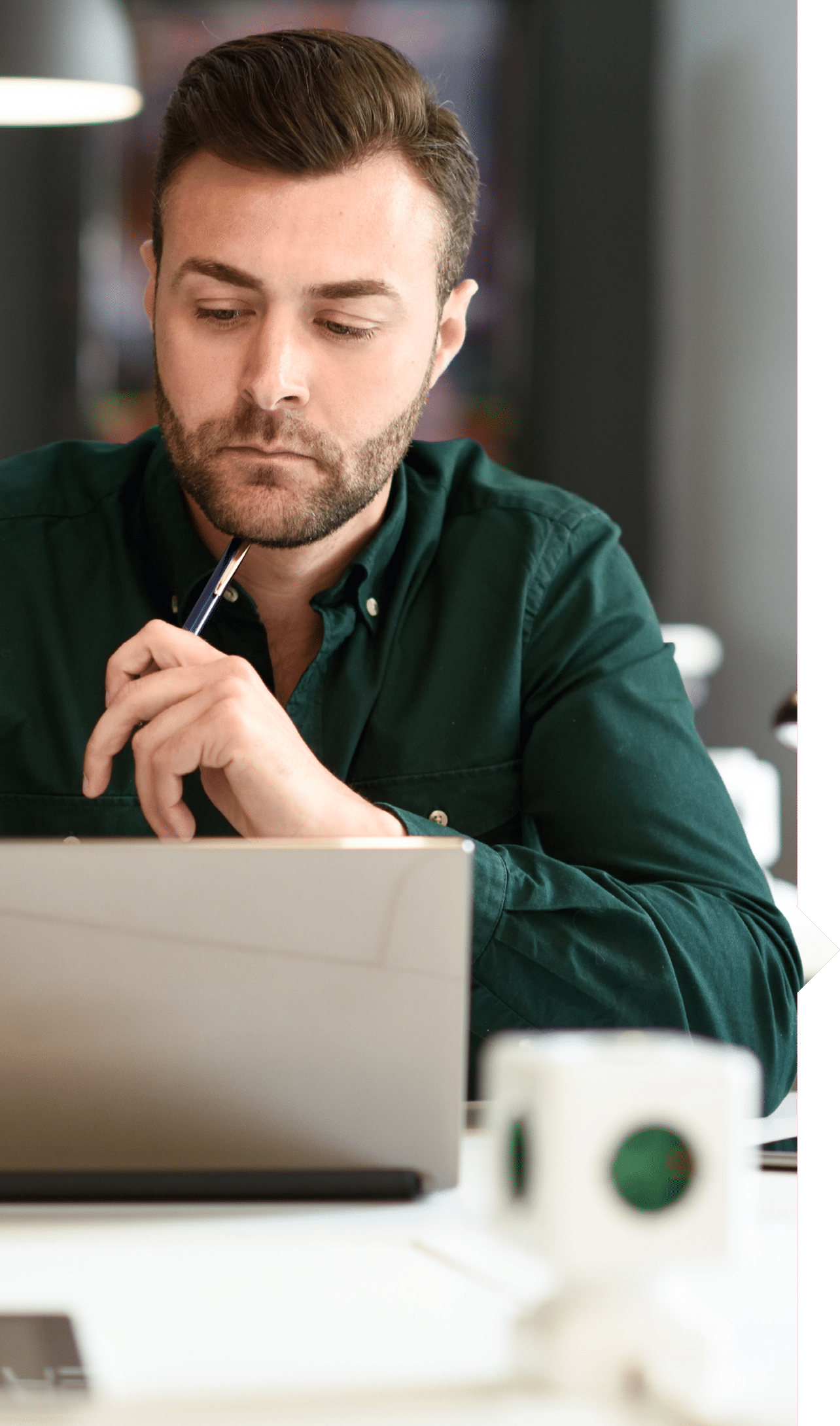 Young man studying with laptop computer on white desk. Attractive guy with beard wearing casual clothes.