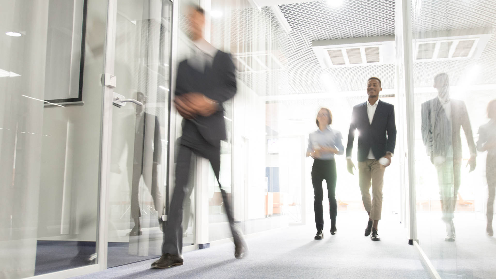 Blurred motion of modern business people crossing illuminated office corridor while hurrying to their workplaces, corporate company
