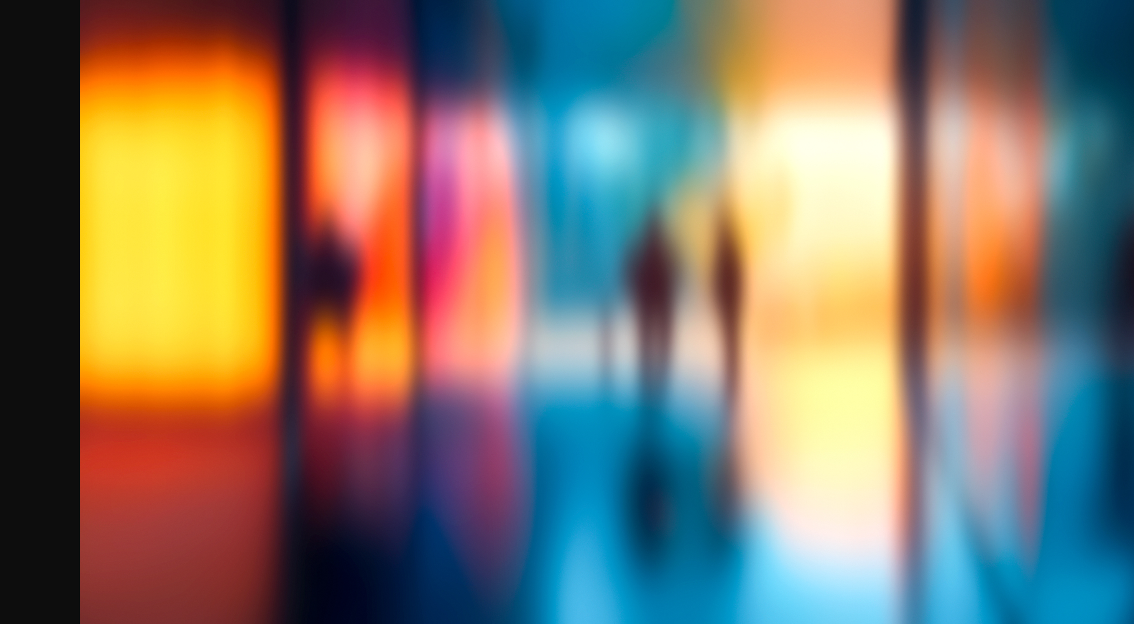 Several blurred figures stand and walk in a colorful, abstract environment with warm and cool light panels. Description generated by AI