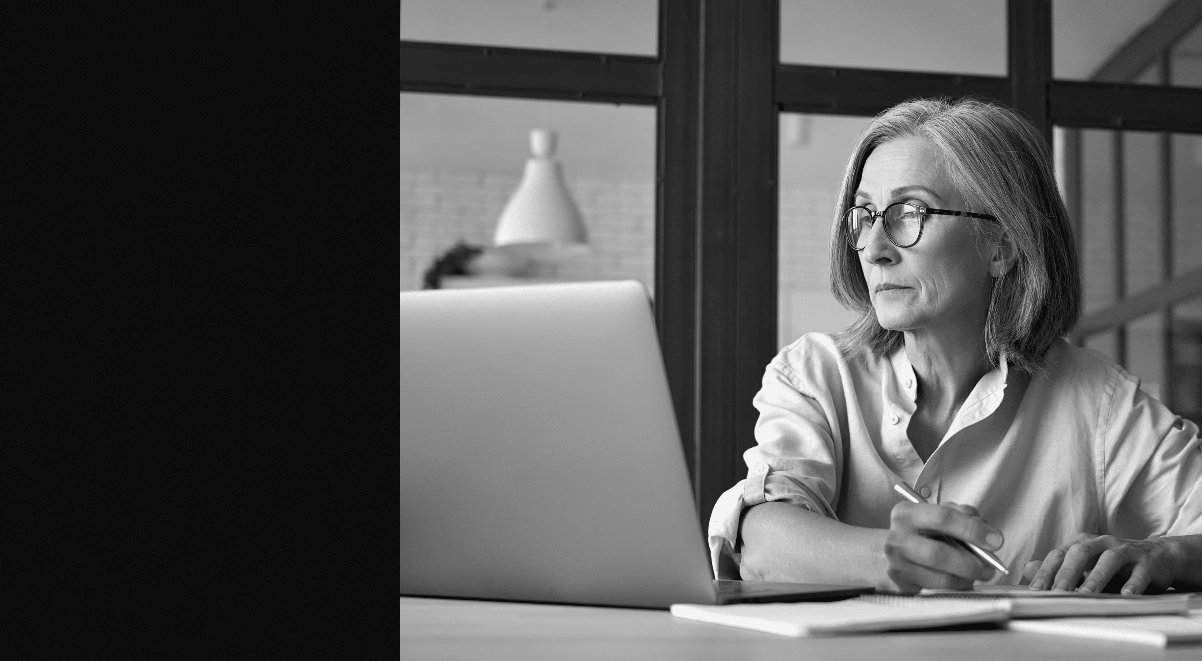 Serious mature older adult woman watching training webinar on laptop working from home or in office. 60s middle aged businesswoman taking notes while using computer technology sitting at table.